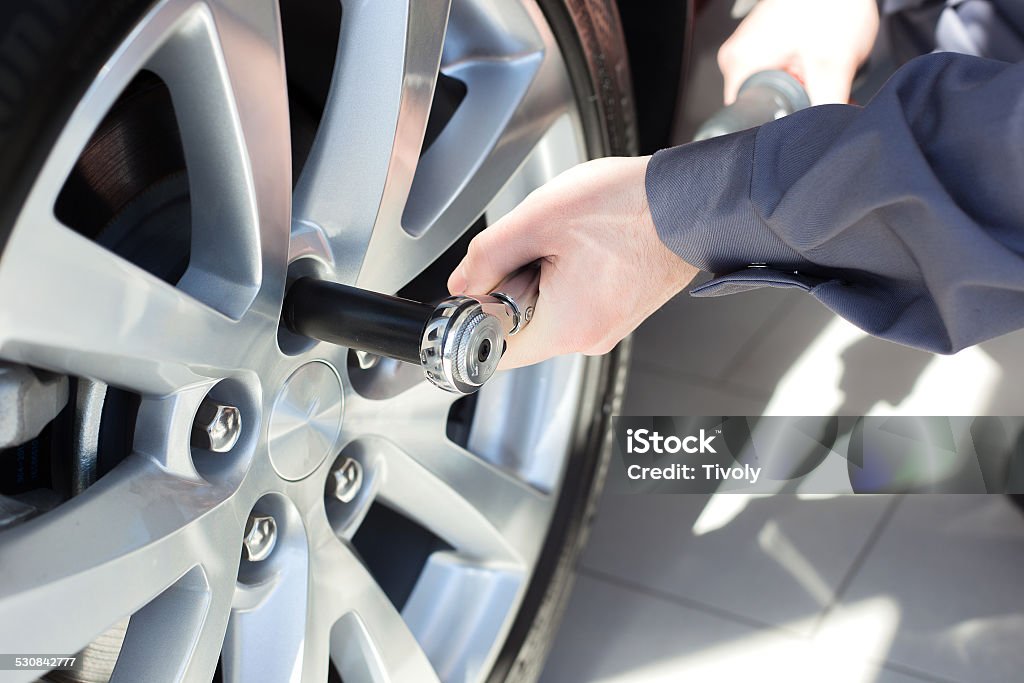 Mechanic changing wheel on car Mechanic changing wheel on car with a wrench Adult Stock Photo