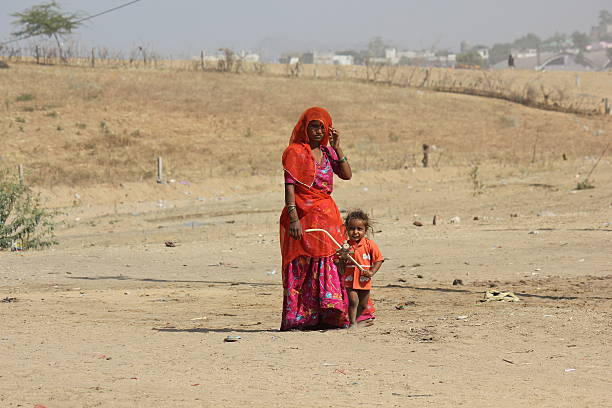 Pushkar, India, November 28 2012: A poor Indian Mother orange dressed with her son, standing on the sand of the arid city of  Pushkar