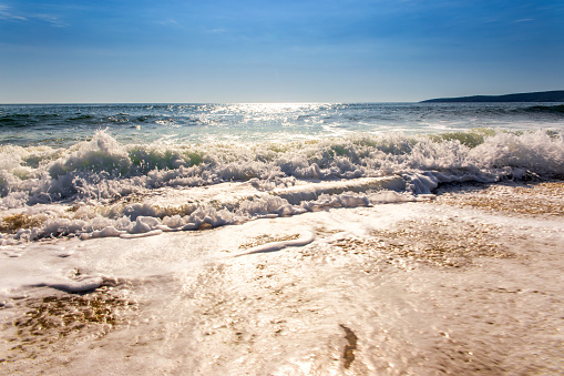 sand sea beach and blue sky after sunrise and splash of seawater with sea foam and waves