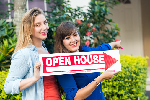 Young Female realtors holding an open house sign at a residence front entrance