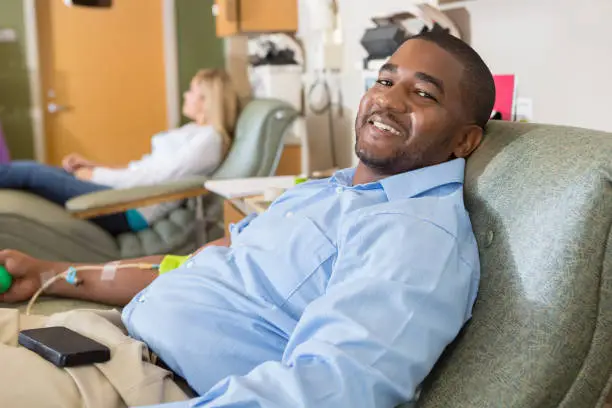 Happy African American man donating blood in hospital lab