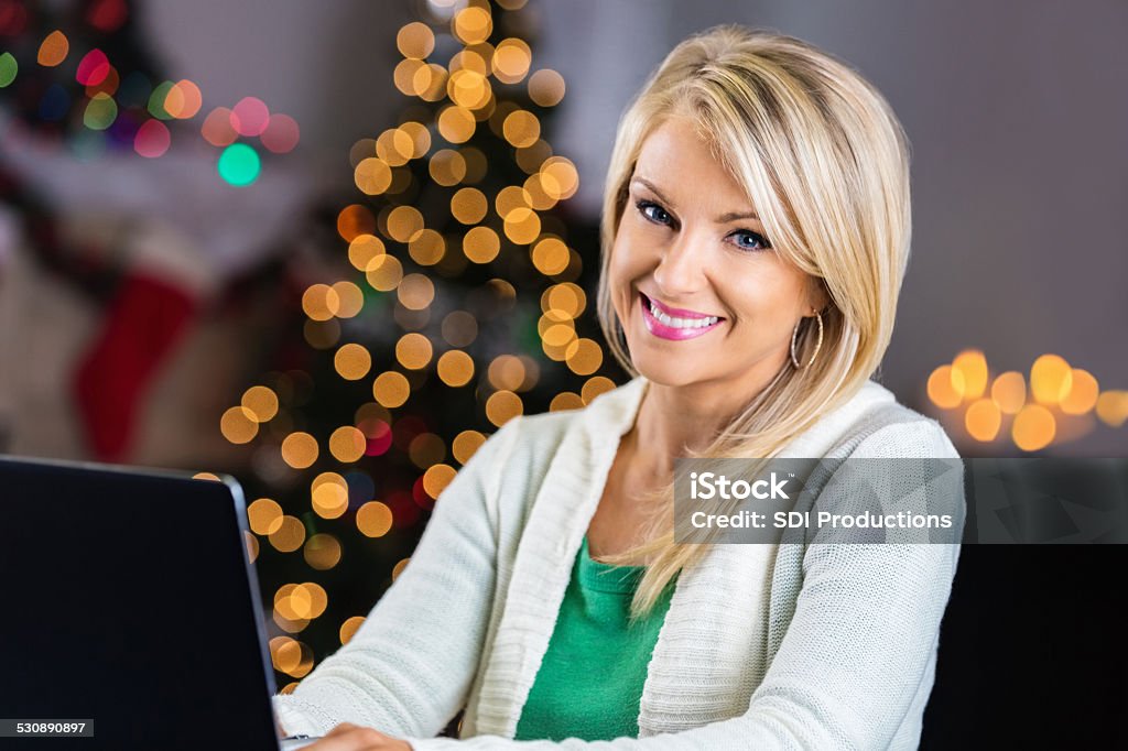 Beautiful blonde woman using laptop at home during Christmastime Adult Stock Photo