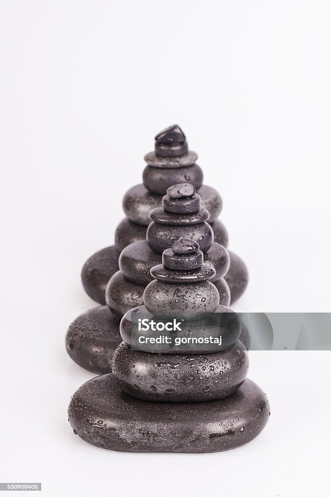Spa stones isolated on white Row of seven chakra colored crystals lined in a row on wet smooth polished hot massage black stones Alternative Therapy Stock Photo