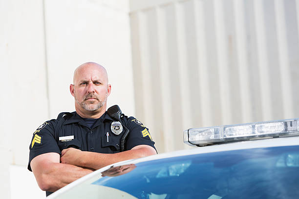 istock Serious police officer standing next to cruiser 530916489