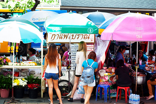 Bangkok, Thailand - November 8, 2014: Capture of Thai women standing at different market stalls at Victory Monument. At left side a woman is selling buddhist flowers. In center is a person sellig drinks. At right side is market stall with food. Some people are sitting at right side.