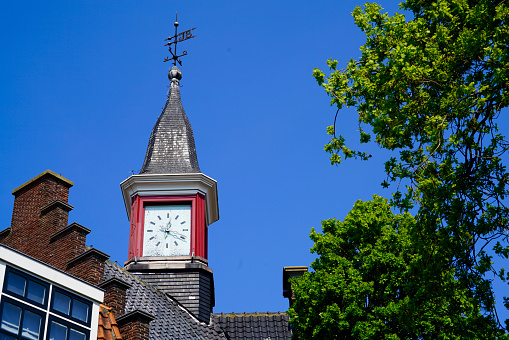 steeple with a red clock in front of a perfect blue sky and a green tree aside