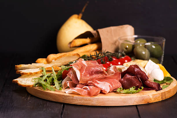 Various types of italian appetizers: ham, cheese, grissini, olives, fruits Various types of italian appetizers: ham, cheese, grissini, olives, fruits over black wooden background. Selective focus antipasto stock pictures, royalty-free photos & images