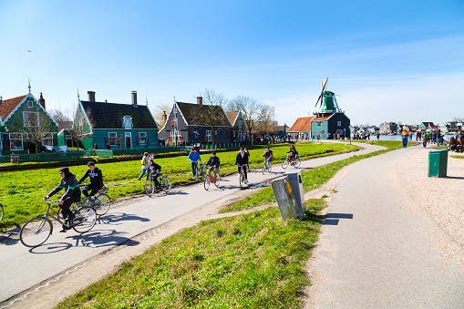 Zaanse schans, Netherlands - April 1, 2016: People riding bicycles, green windmill in Zaanse Schans, Holland, traditional village, blue sky