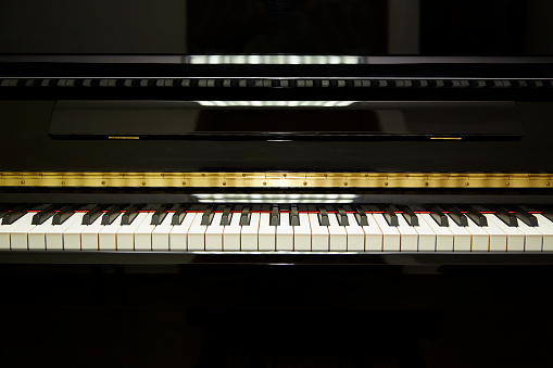 Black upright piano keys, facing the camera with close shot. black on upper and lower part of the images with white and black keys in the third of the image. great for adding text or logo.