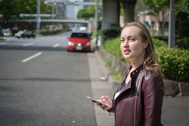 Young White Female Waiting For Taxi A young white female wating on the roadside in central Tokyo, for a taxi or ride. low angle street japan stock pictures, royalty-free photos & images