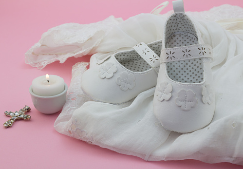 Baby girl shoes, cross and candle on white lace with pink background