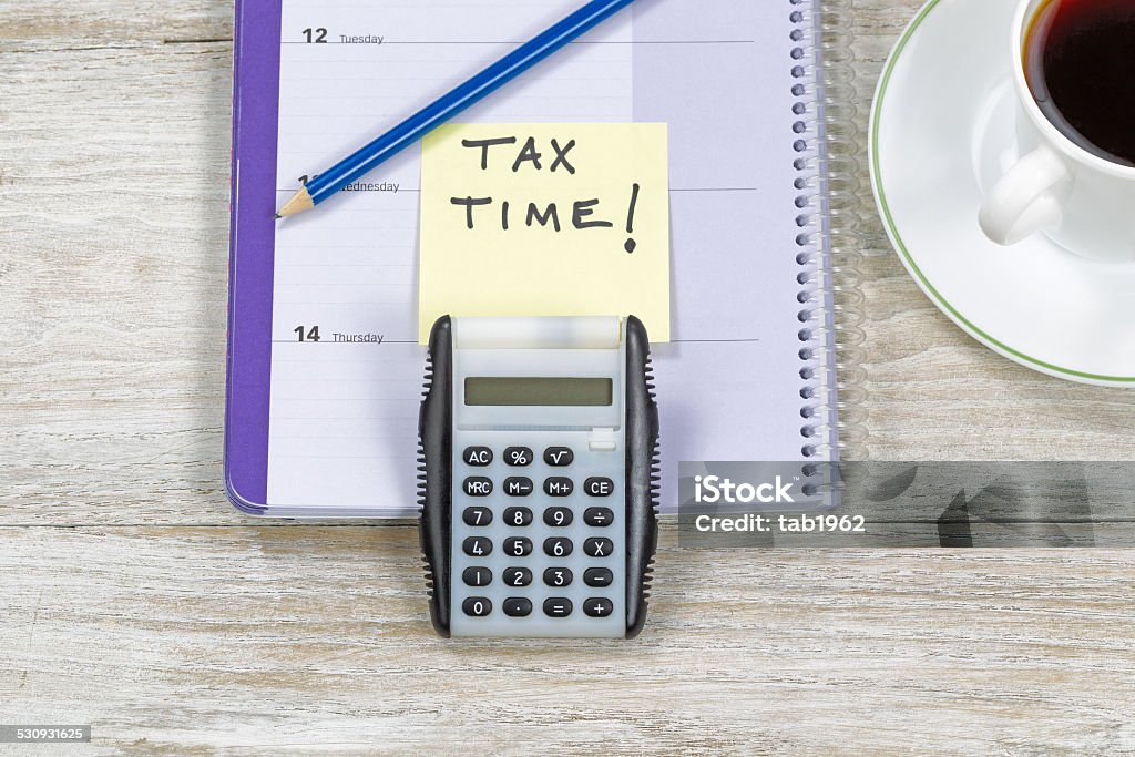 Doing Income Taxes Horizontal top view of an office wooden desktop with small calendar, calculator, coffee and sharpen blue pencil with reminder of doing Tax Returns. Above Stock Photo