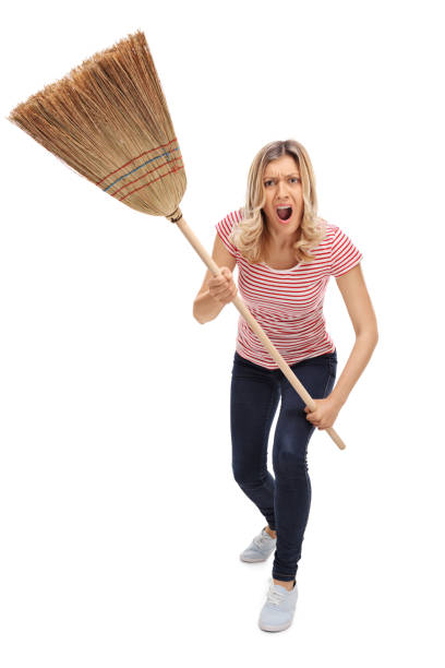 Vertical shot of an angry woman threatening with a broom and shouting towards the camera isolated on white background