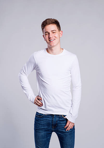 Boy in jeans and t-shirt, young man, studio shot Teenage boy in jeans and white long sleeved t-shirt, young man, studio shot on gray background long sleeved stock pictures, royalty-free photos & images