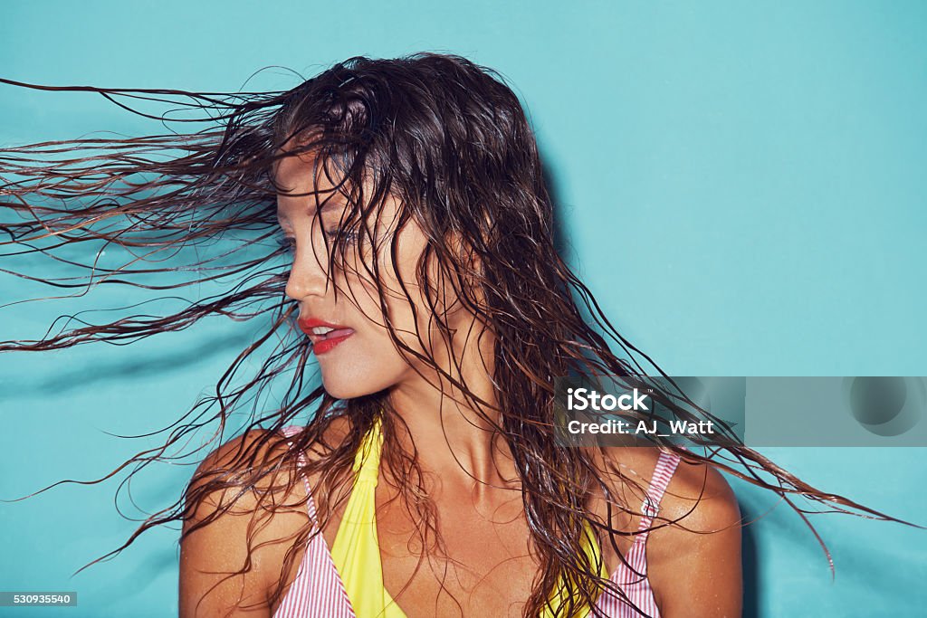 There's just something about wet hair... Shot of a young woman flipping her wet hair against a blue background Wet Hair Stock Photo