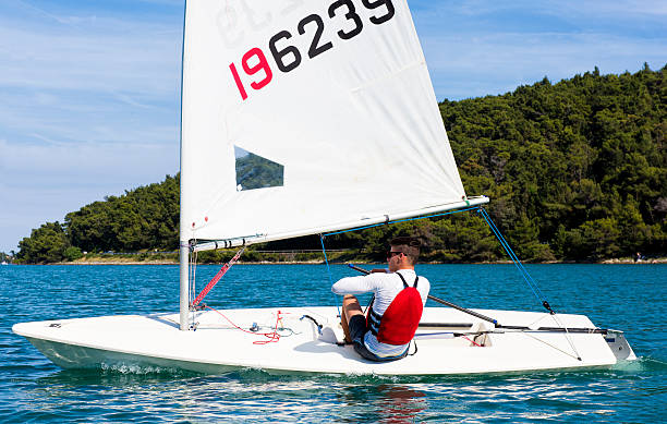 Young man sails a laser class sailing boat Side view of young male boats-man sailing on laser class sailing boat sailing dinghy stock pictures, royalty-free photos & images