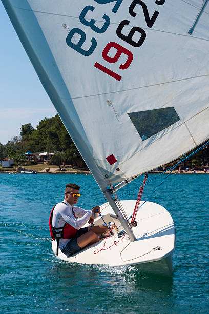 International laser class sailing boat with young male boats-man practicing, front view