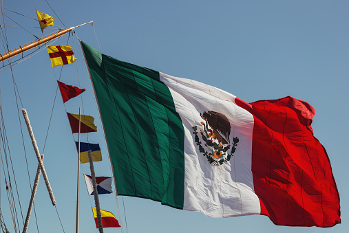 A massive Mexican flag hangs from the masts of a tall ship.