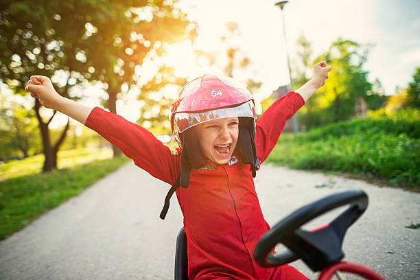 Portrait of happy little boy winning a go-kart race Little boy aged 6 has won a a pedal go-kart race (or kart, soapbox car, cyclekart race). Little boy is happily rising his arms in winning gesture. Road and sunset visible in the background. soapbox cart stock pictures, royalty-free photos & images