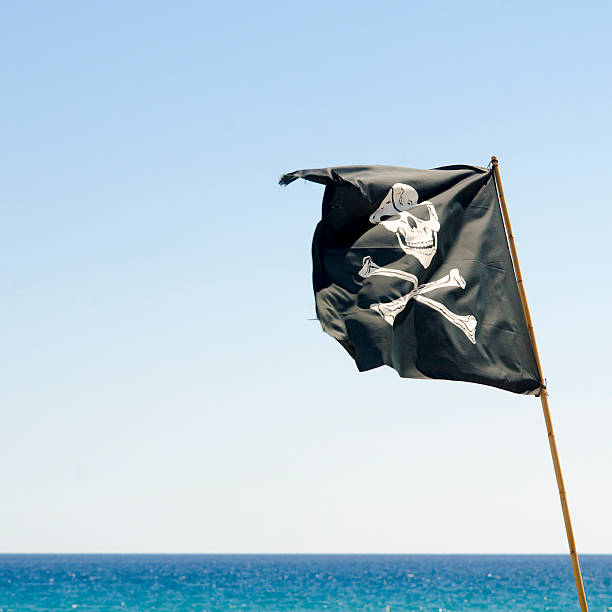 istock pirate flag waving with blue sea background 530945927