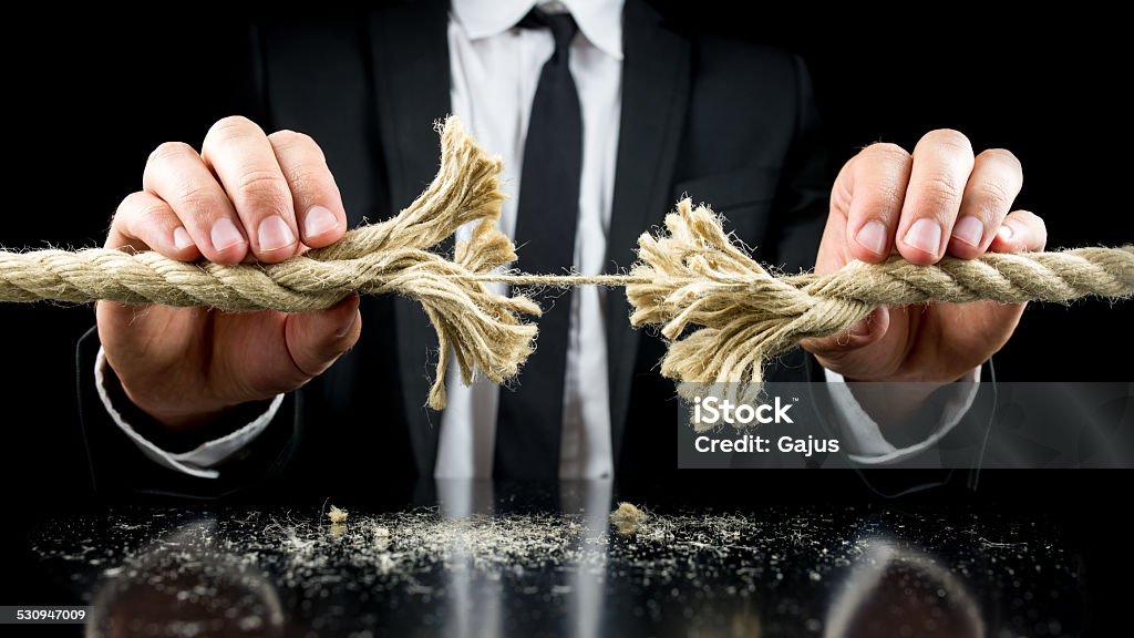 Risk and adversity concept Businessman holding a frayed rope with one remaining string intact in both his hands in a risk and adversity concept. Over black background. Rope Stock Photo