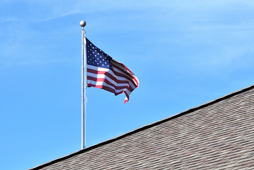 US flag flying behind building roof.