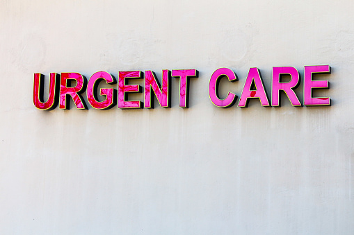 Signage for Urgent Care, red elevated letters against beige wall.  Exterior sign.  Urgent care is a commonly used part of the healthcare system in the United States.