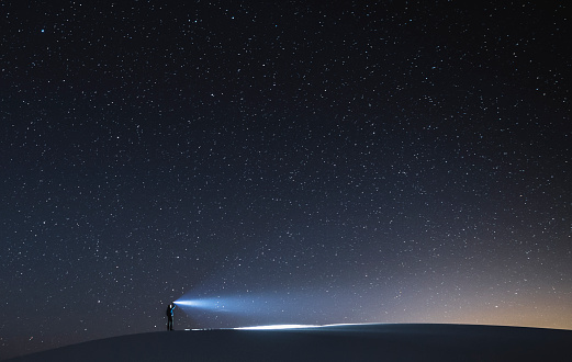 Person standing on the dune with a flashlight during the night looking for answers, White Sands National Monument, New Mexico.