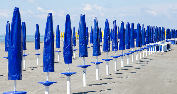 sandy beach with rows of closed sun umbrellas in blue protective covers at Grado, Italy