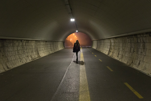 Young woman walks alone in the night trough a dark tunnel. 