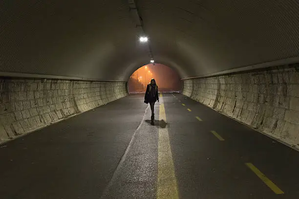 Photo of Young lady walks alone trough a tunnel in the night