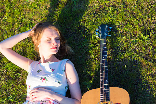 Beautiful hippie girl with guitar lying on the grass