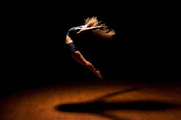 Beautiful dancer jumping in a stage Full length profile view of a gorgeous female jazz dancer jumping during a performance in a dark stage under a spotlight ballerina shadow stock pictures, royalty-free photos & images