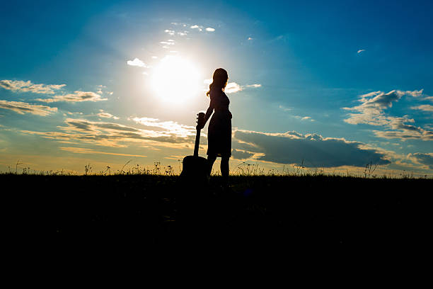 A woman sitting in a park holding a black guitar excited about the sight