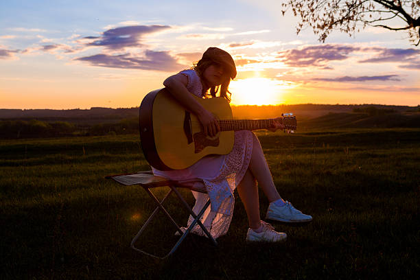 istock Beautiful young woman playing guitar at sunset 531003048