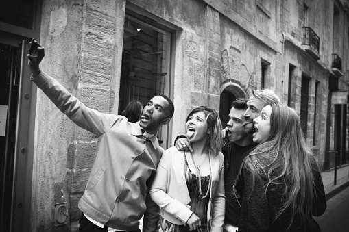 Group of friends with shopping bags taking selfie on the streets of Paris, France.