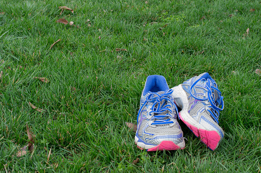 Pair of old running tennis shoes  on green grass. Though running is considered a cheap exercise, runners go through a new pair of running shoes every 300 miles
