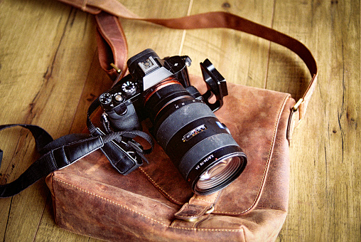35MM Camera with lens lying on a rustic brown carrying bag on a wooden table top.