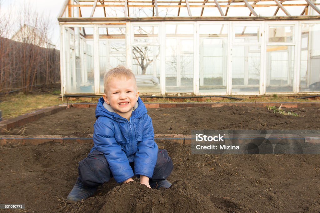 Little farmer Happy smiling joyful child (boy) digging soil, working in spring garden in village. Little farmer. 2015 Stock Photo