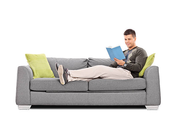 rilassata giovane ragazzo leggendo un libro sul divano - reading book men sofa foto e immagini stock
