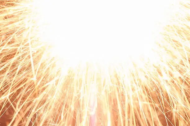 Burning sparkler in front of a dark background.