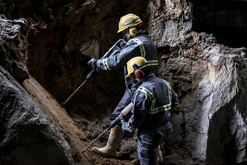 Two workers with helmet and protective suit using drill-machines in an underground enviroment