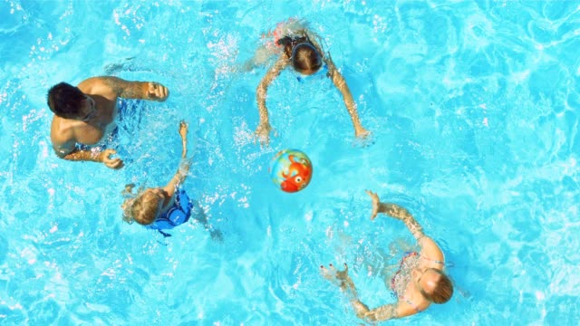 A young family playing ball in the pool on a sunny day