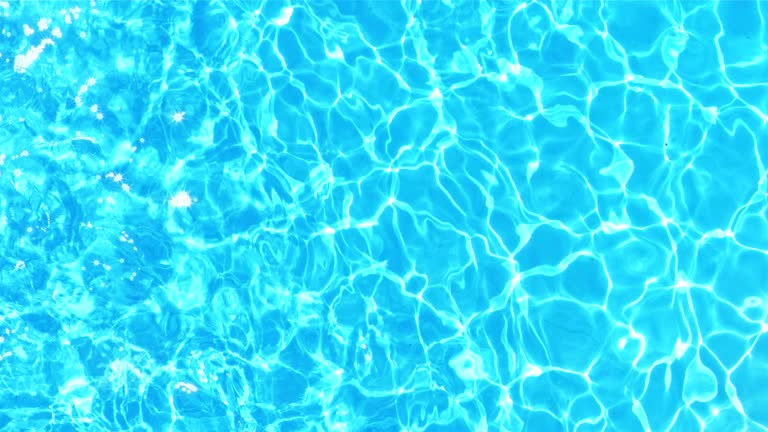 Slow motion wide crane shot of the crystal clear water shining in the pool on a sunny day.