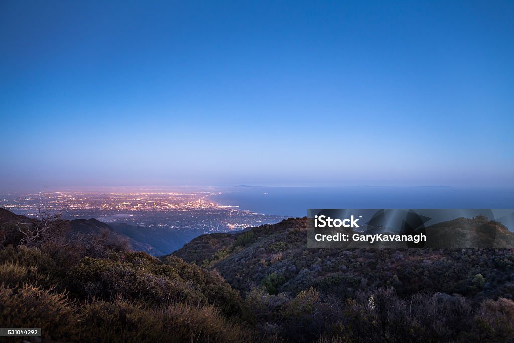Santa Monica Bay & Westside of Los Angeles From Mountains The Santa Monica Bay & the city lights of Santa Monica and the Westside of Los Angeles glowing at dusk with a clear sky and soft marine layer rolling into the basin. View is from the Temescal Canyon ridgeline trail in the Santa Monica Mountains. Pacific Palisades Stock Photo