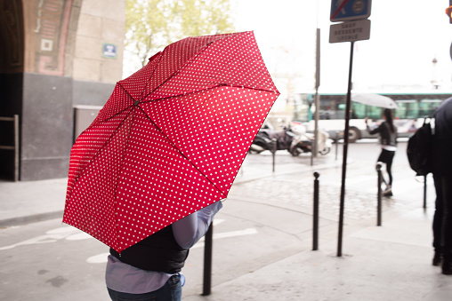 An unrecognisable person walks along a street in downtown Paris, with her umbrella protecting her from the rain. There are spots of rain on the umbrella
