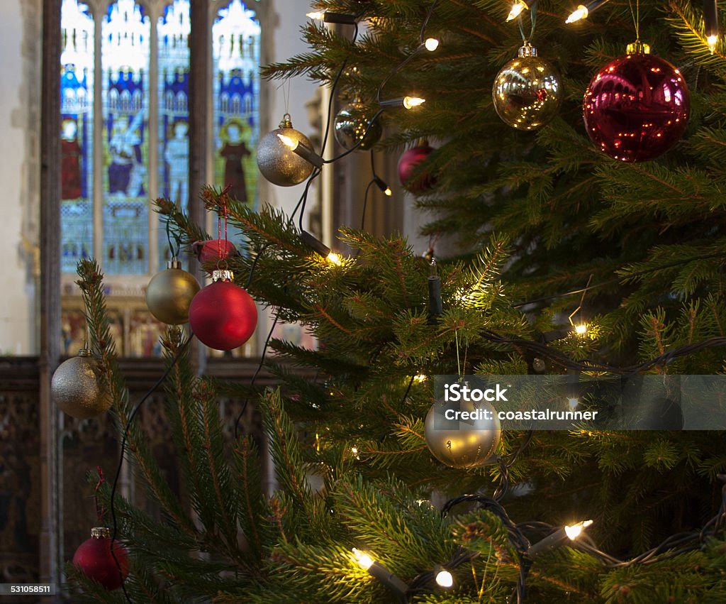 Decorated Christmas tree in an English church Interior of an English church at Christmas, with a fresh tree hung with red and gold baubles and clear lights. Focus on the baubles, throwing the stained glass window behind the altar into soft focus. Church Stock Photo