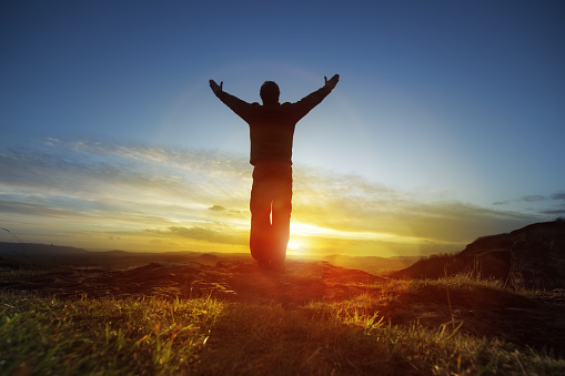 Silhouette of a man with hands raised in the sunset concept for religion, worship, prayer and praise