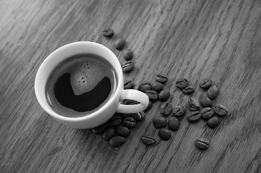 Black and white image of an espresso coffee, beans and coffee pot on a wooden table background