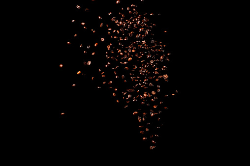 Flying coffee beans isolated on black background. Roasted coffee grains explosion.